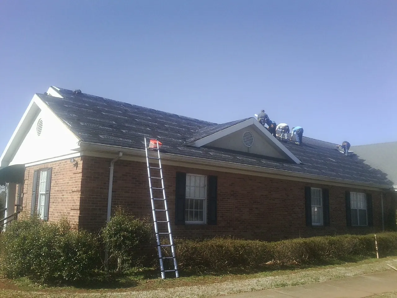 Crew tearing shingles off a brick ranch roof with a ladder set — Metal Roof Repair work by our crew in Kimmell