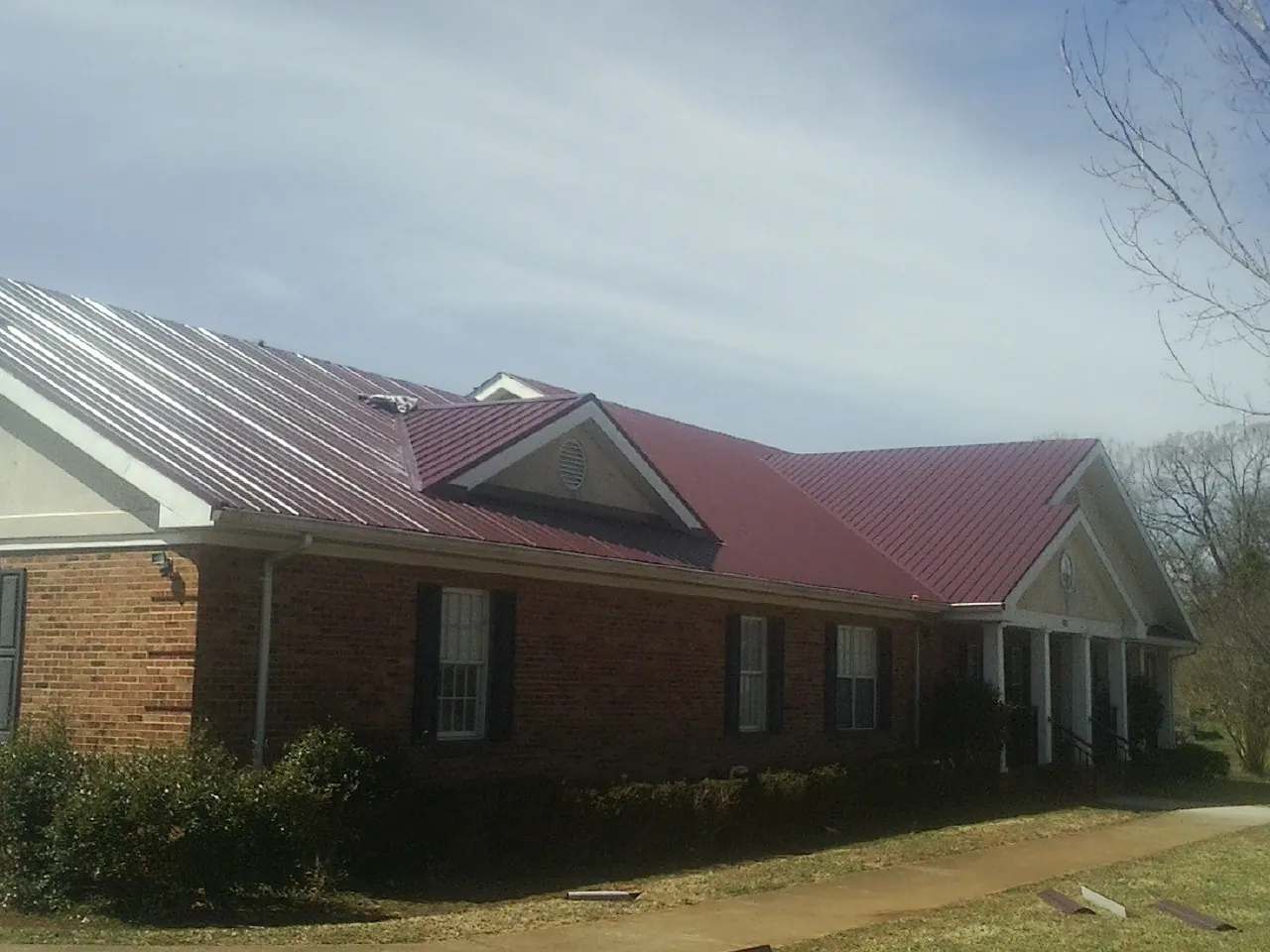 Red metal roof with gabled entries on a long brick building, from a Hail Damage Roof Repair job in Kimmell