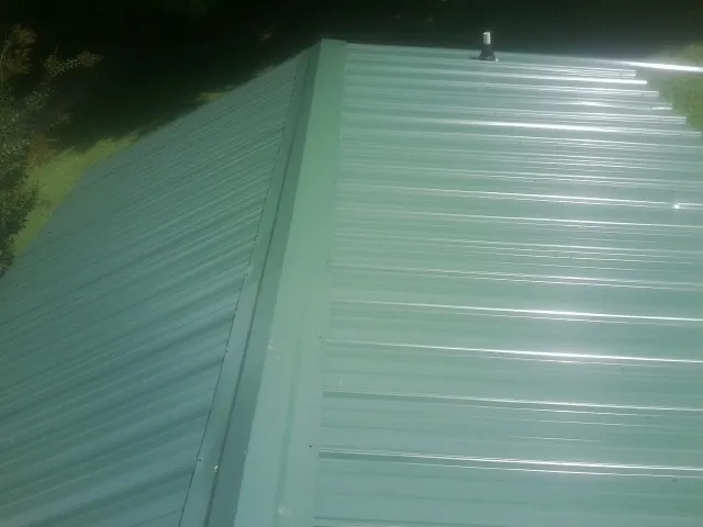 New green metal panels meeting at the ridge of a roof — Flat Roof Repair work by our crew in Kimmell