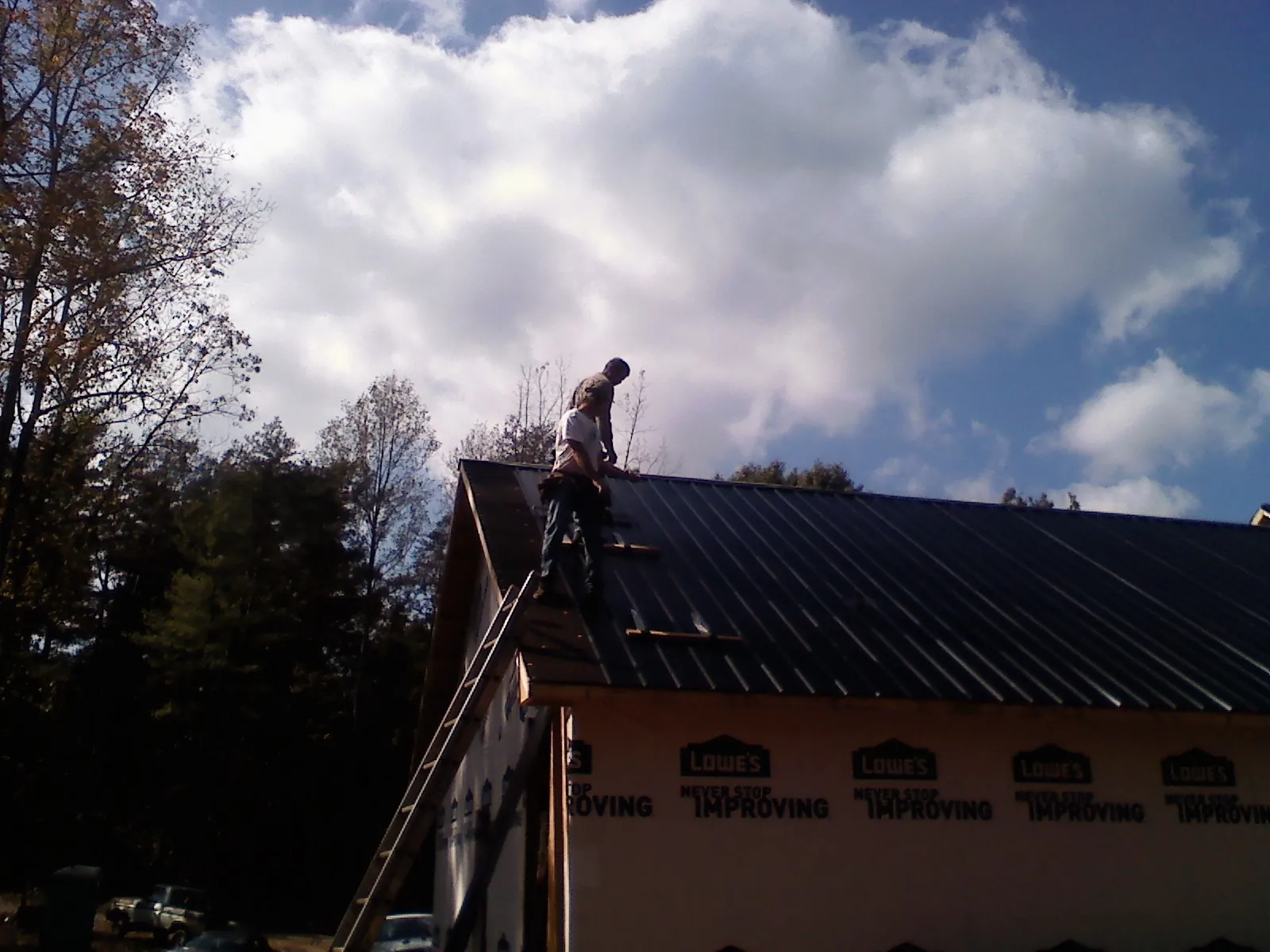 Roofer fastening dark metal panels high against a cloudy sky, from a Roof Inspection job in Kimmell