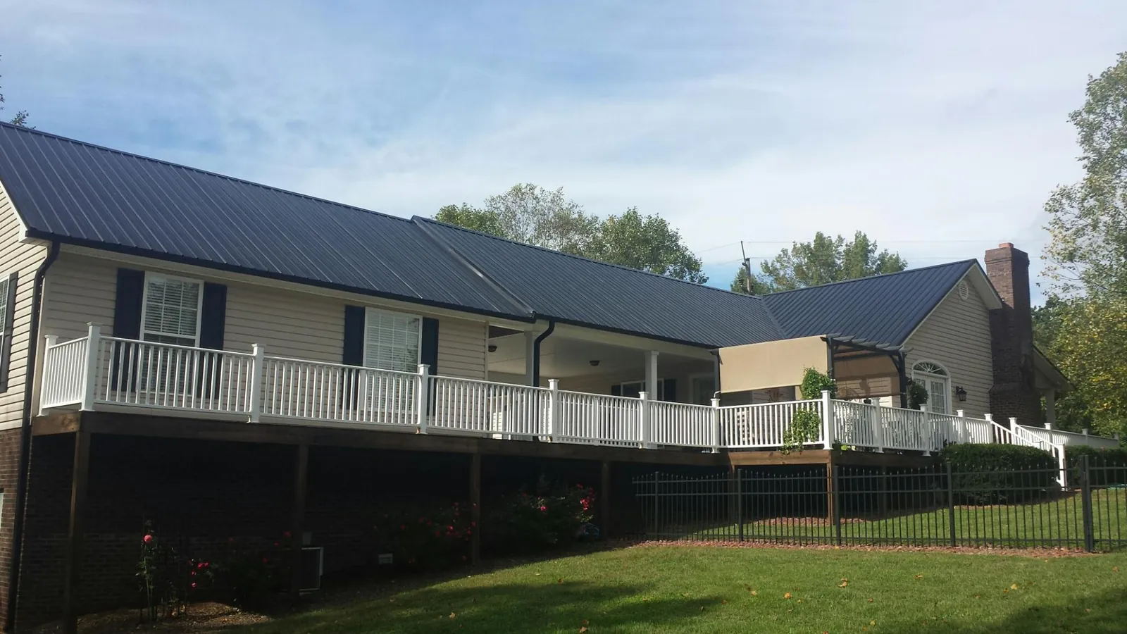 Black metal roof above a long white railed deck on a hillside home in Kimmell