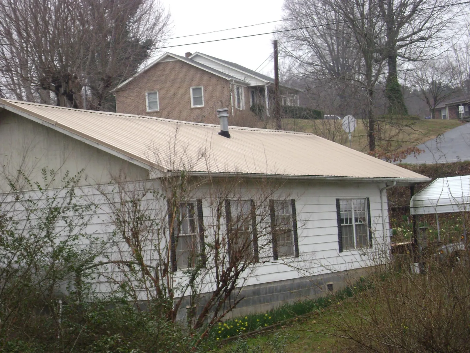 Tan metal roof on a white sided house set into a hillside — Commercial Roofing by Roofing Brothers in Kimmell